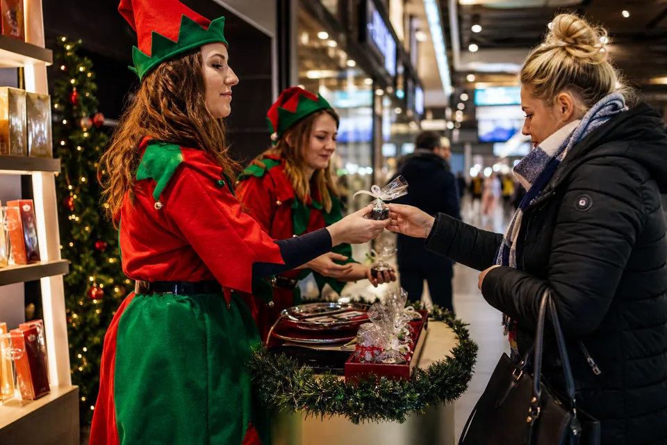 Hostessy w strojach elfów wręczają klientce upominek przy stoisku w pasażu galerii handlowej